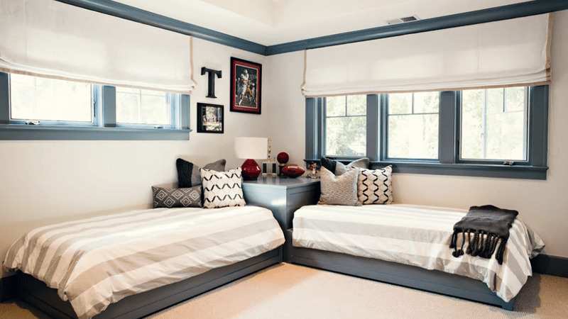 A small bedroom with L shaped bed with windows and wooden floor