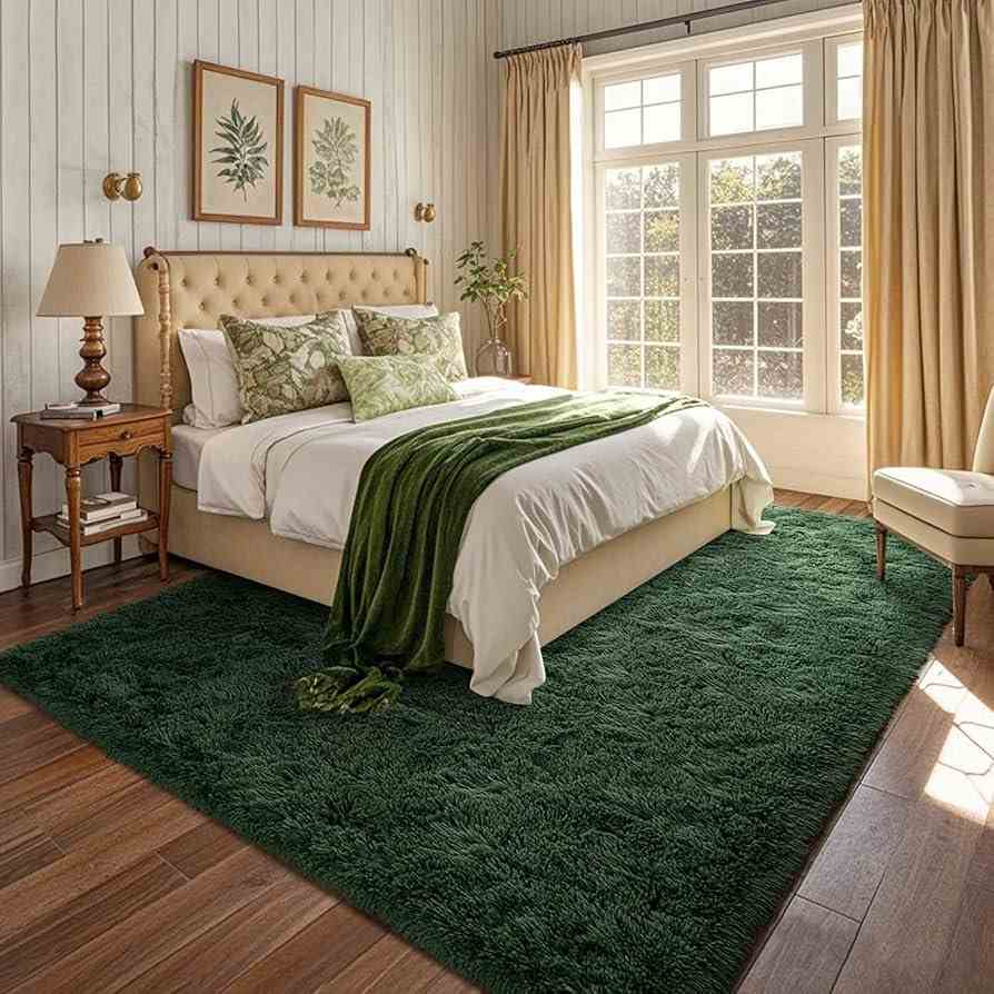 A bedroom with green rug on wooden floor and frames on the wall 