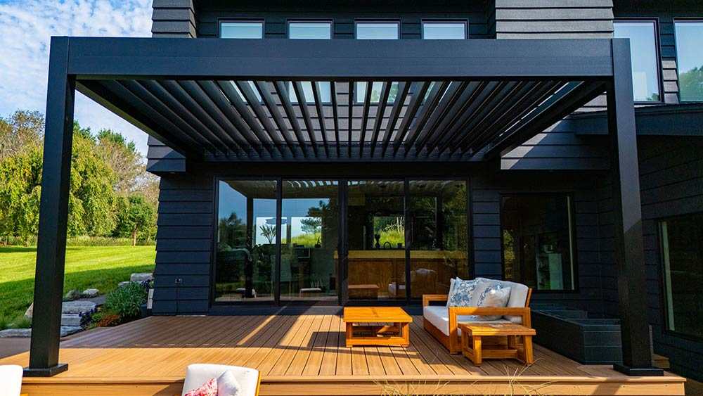 A charcoal grey house with black pergola and wooden floor 