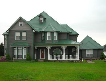 A dark grey house with green roof and white trim and garden outside of the house
