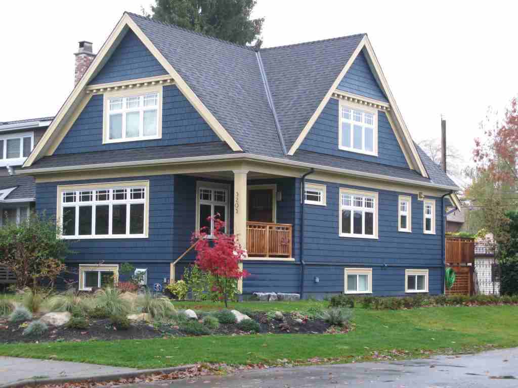 A blue house with grey roof and white windows and wooden balcony 