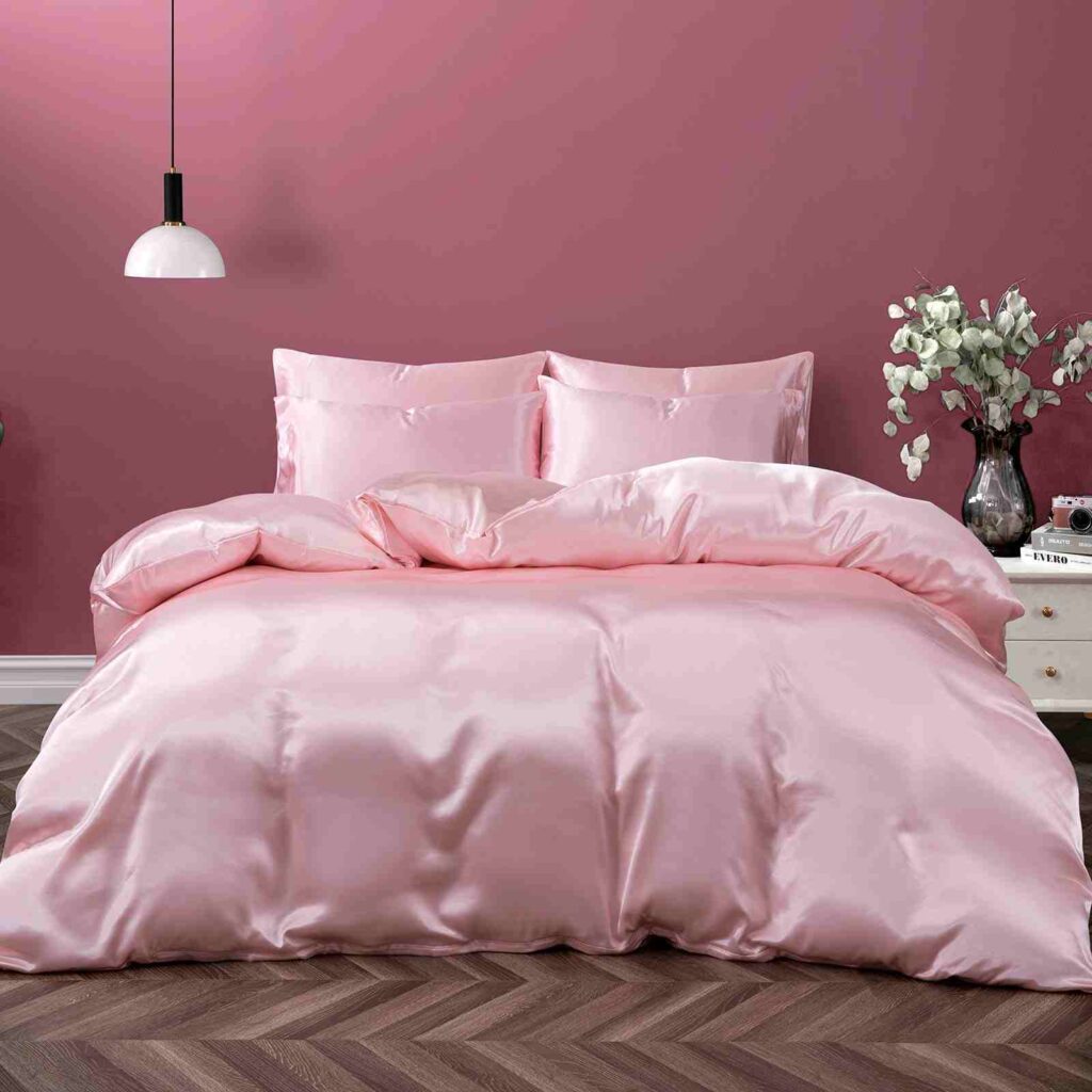 A pink bedroom with pink satin blankets and pillow and wooden floor