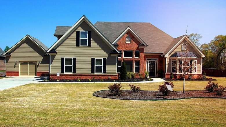 A sage green house with brick and white trim windows and black shutter 