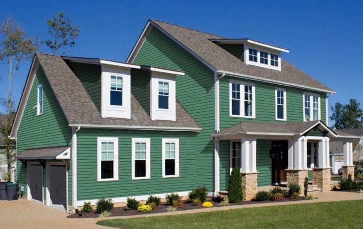A dark green house with white trim and black roof and garden outside of the house 