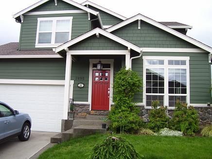 A green house with white trim and red door and glass windows