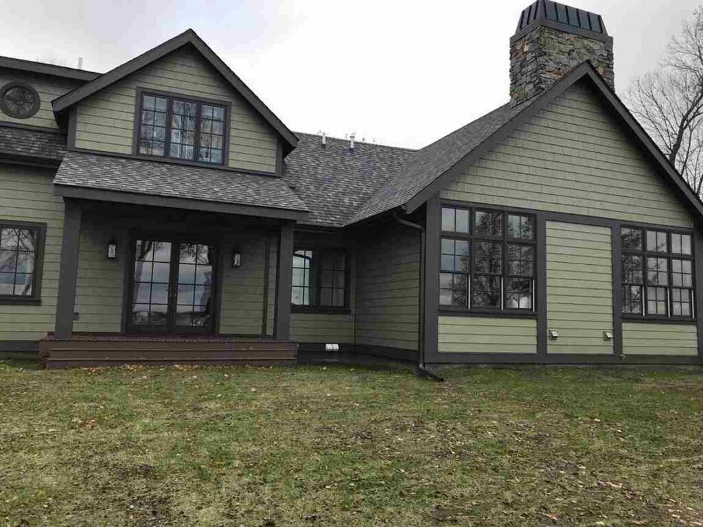 A dark olive house with black trim and stone chimney and glass windows