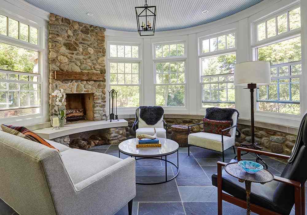A sunroom with stone base fireplace and floor and sofa with table 