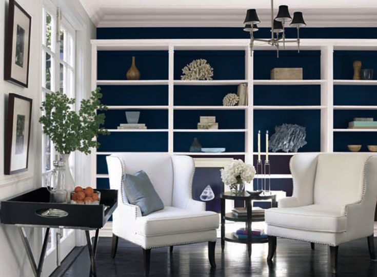 A navy blue living room with white open shelves and chair ad table