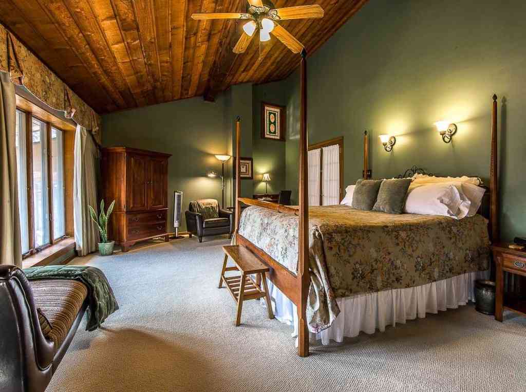 A green bedroom with wooden celling and bed and lights above the bed 
