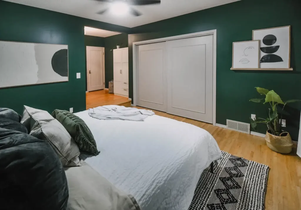 A forest green bedroom with wooden floor and frames on the wall 
