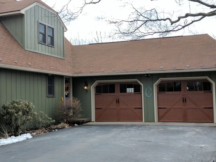 A green house with wooden garage door and brown roof
