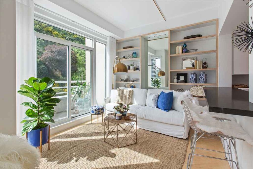 A living room with plants and windows and wooden floor and built shelves 