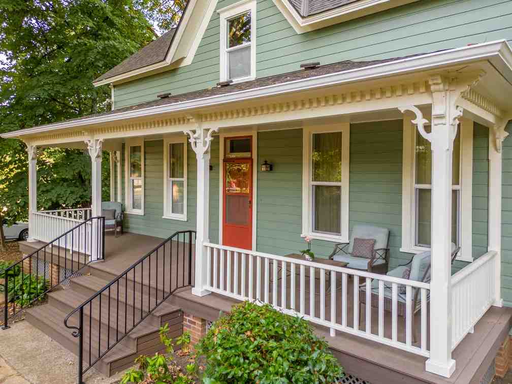 A light green hpuse with wooden porch and red door and white trim 