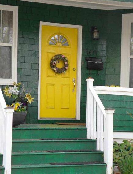 A green house with yellow door and white trim 