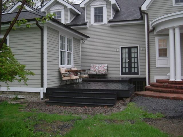 A black decking with light grey house with window and garden outside of the house