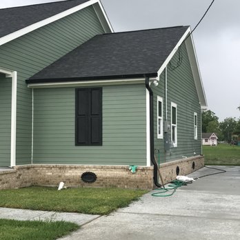 A green house with black gutter and white windows and pathway 