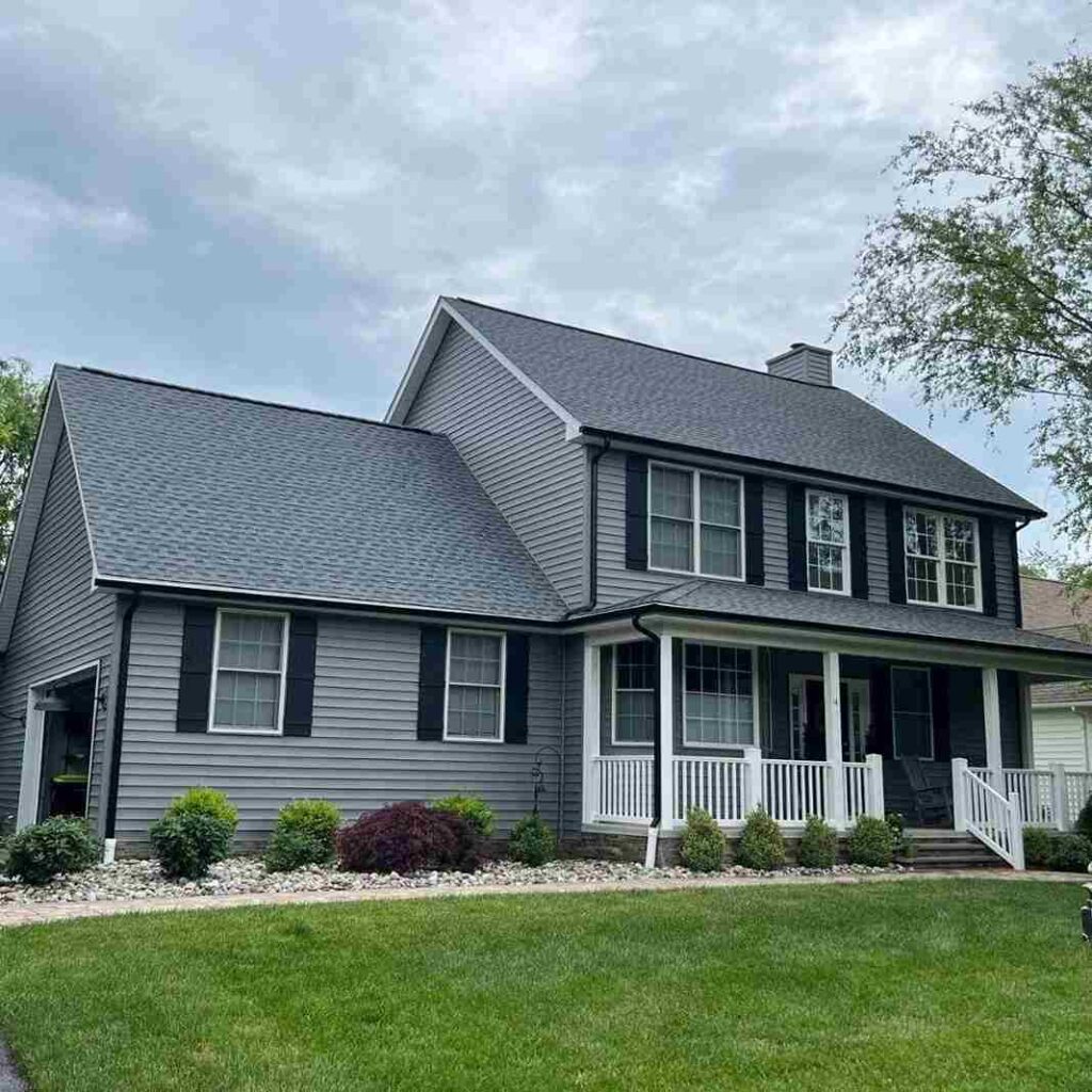 A grey house with white trim and black shutters and garden outside of the house 