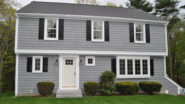 A light grey house with black shutter and windows and garden outside of the house
