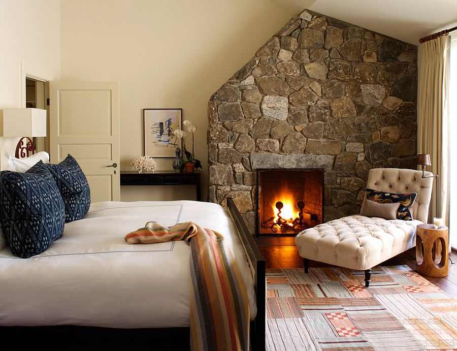 A beige bedroom with stone fireplace and white chair