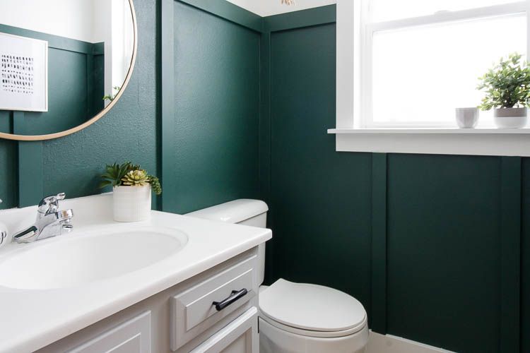 A green bathroom with wainscoting wall and white vanity
