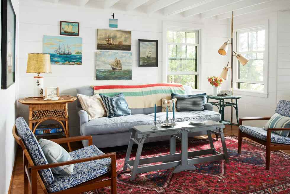 A sunroom with frames on the wall and red rug and chair and table 