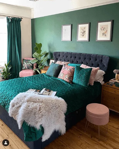 A green bedroom with pink accents and wooden floor and frames on the wall 