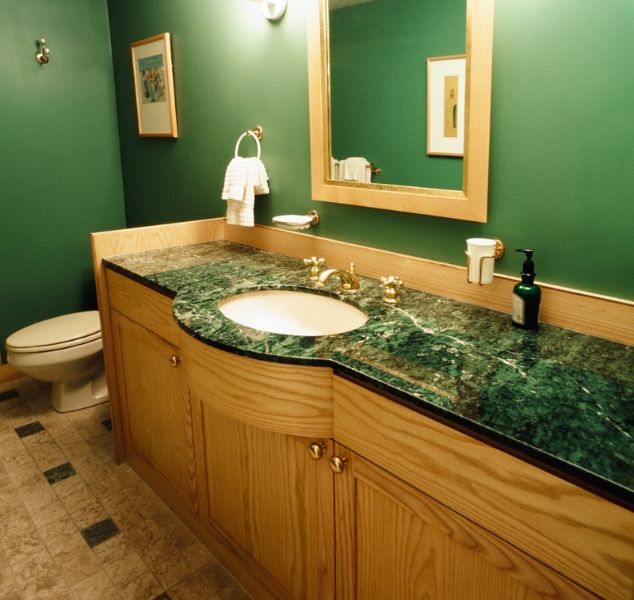 A green bathroom with wooden vanity and green countertop and mirror on the wall
