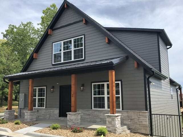 A grey house with wooden trim and stone base pillars and windows