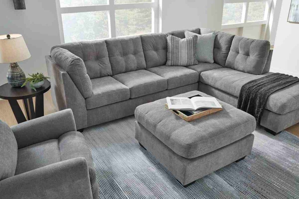 A grey sofa with ottoman in living room with side table and lamp on it 