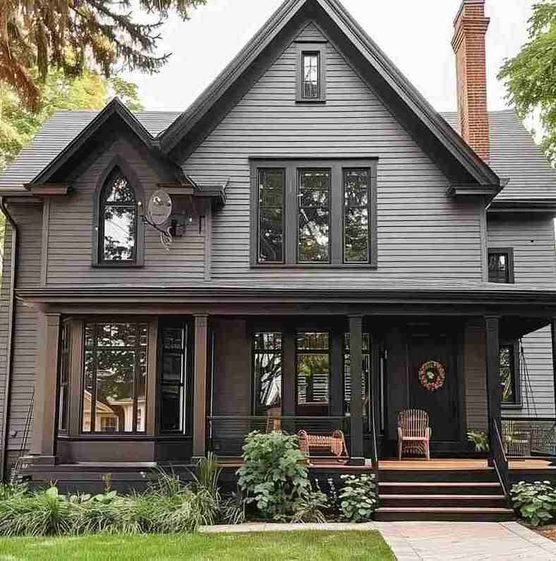 A grey house with black glass windows and black door and wooden floor deck 