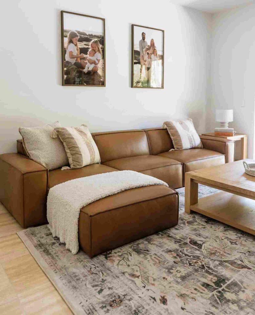 A living room with leather sofa with cushion and throw and wooden floor and frames on the wall 
