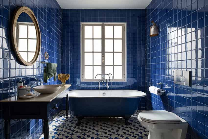 A bathroom with geometric and blue bathtub and windows and gold framed windows  