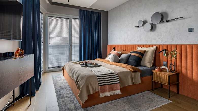 A grey wall with blue curtain and wooden floor and bed