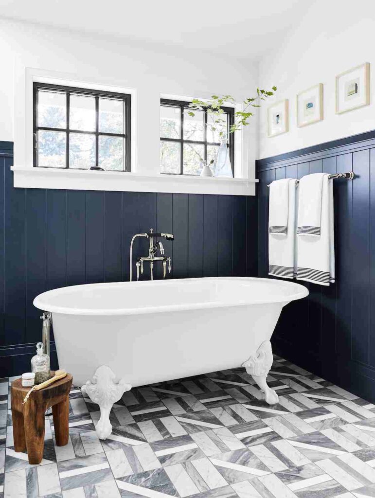 A bathroom navy wainscoting wall and white bathtub and wooden small table and hang towel