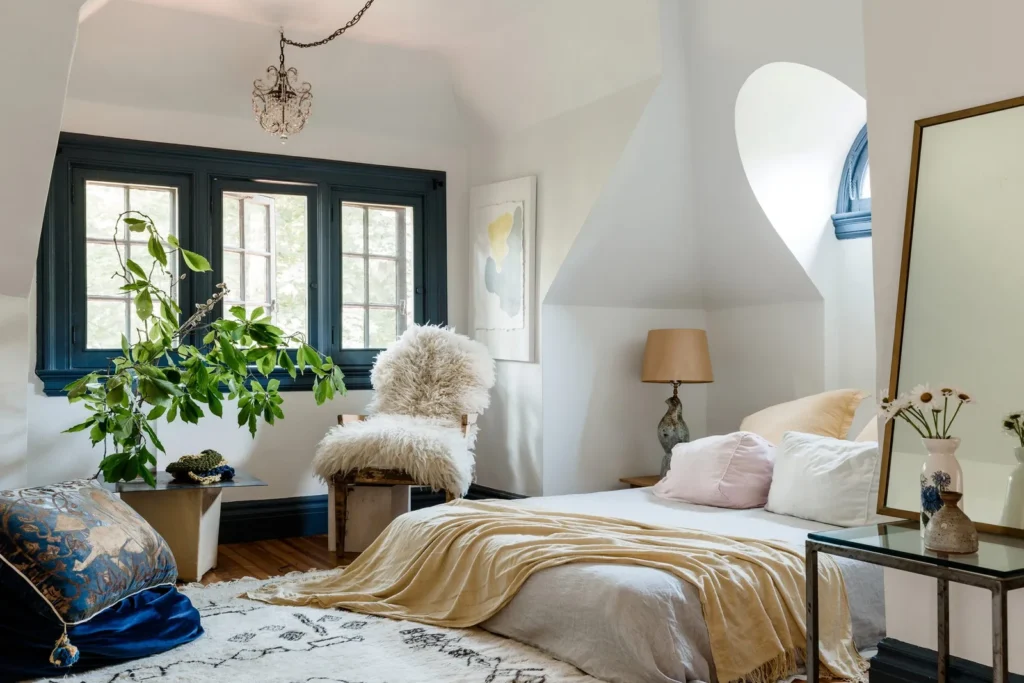 A white bedroom with plant and fur chair and windows