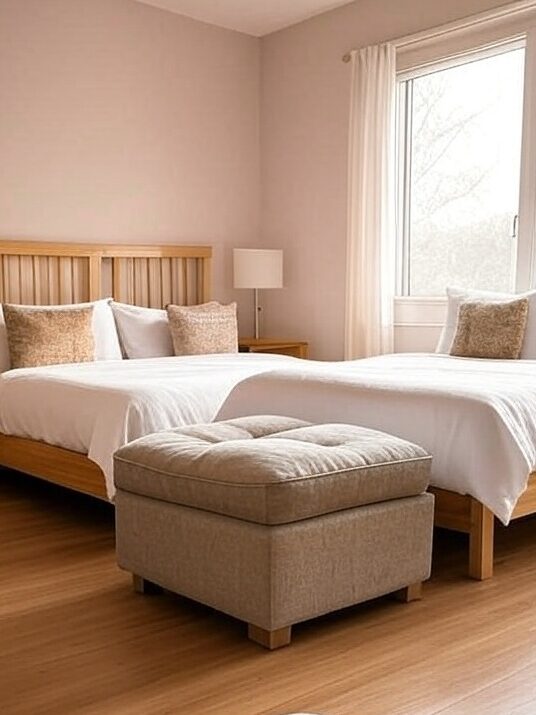 A bedroom with beds and storage ottoman and windows with curtains  