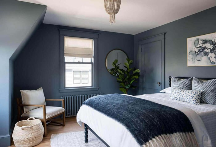 A grey and blue bedroom with windows and wooden floor and chair in the corner