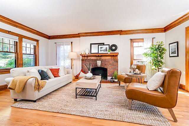 A living room with fireplace and wooden floor and rug on it and windows 