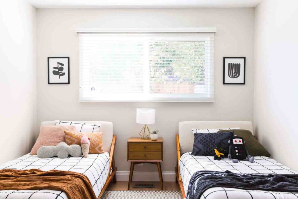 A side by side bed in a room with wooden table and lamp on it and window