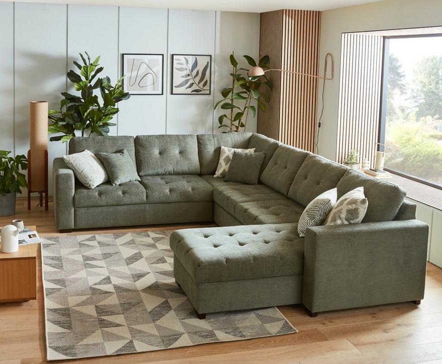 A sage green sofa with ottoman and wooden floor with rug on it 