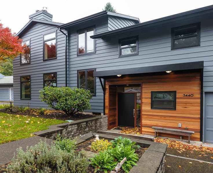 A blue house with black trim and wooden garage door and garden outside of the  house 