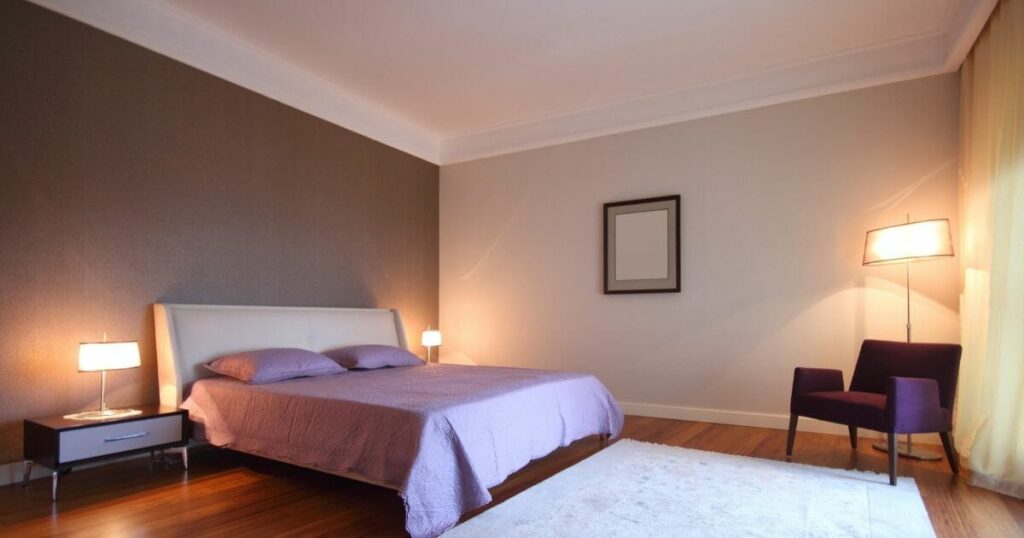 A two tone wall bedroom with lamp on nightstand and wooden floor and rug on it 