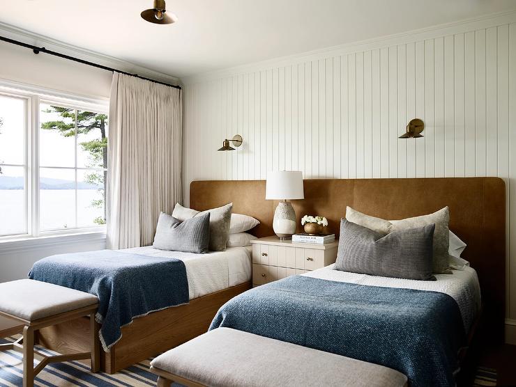 A bedroom with wall sconces and windows with curtains