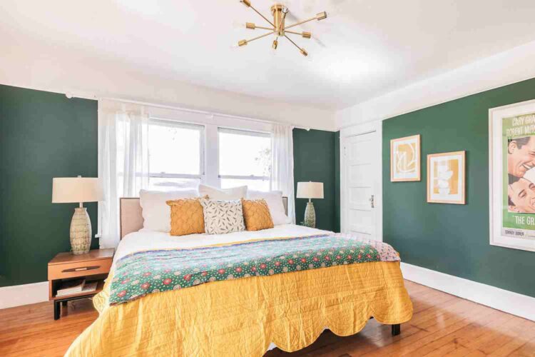 A forest green wall with white trim and wooden floor and lamp on the nightstand 