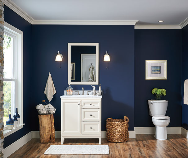 A navy blue bathroom with white vanity and lights on the wall 