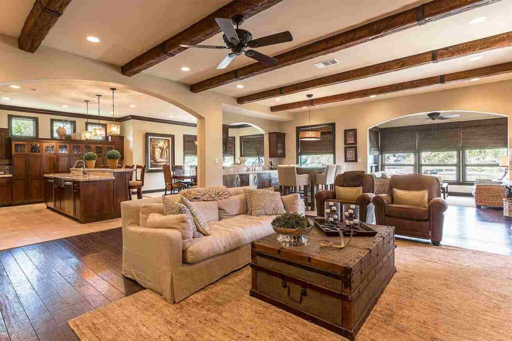 A living room with wooden beams celling and sofa ith cushion and table and rug on the floor 